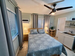 A bedroom with a bed, bedside lamps, a ceiling fan, and a window with blinds. - Pompano Vibes Beach Apartments - Unit 3 "Pelican's Nest" (Pompano Beach)