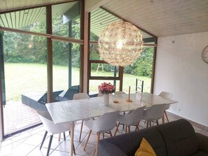 A dining area with a table and chairs, a hanging light fixture, and a view of a garden. - 8 Person Holiday Home in Oksbol (Oksbol)