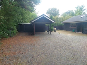 A gravel driveway leading to a wooden structure with a pitched roof, surrounded by dense foliage. - 8 Person Holiday Home in Oksbol (Oksbol)