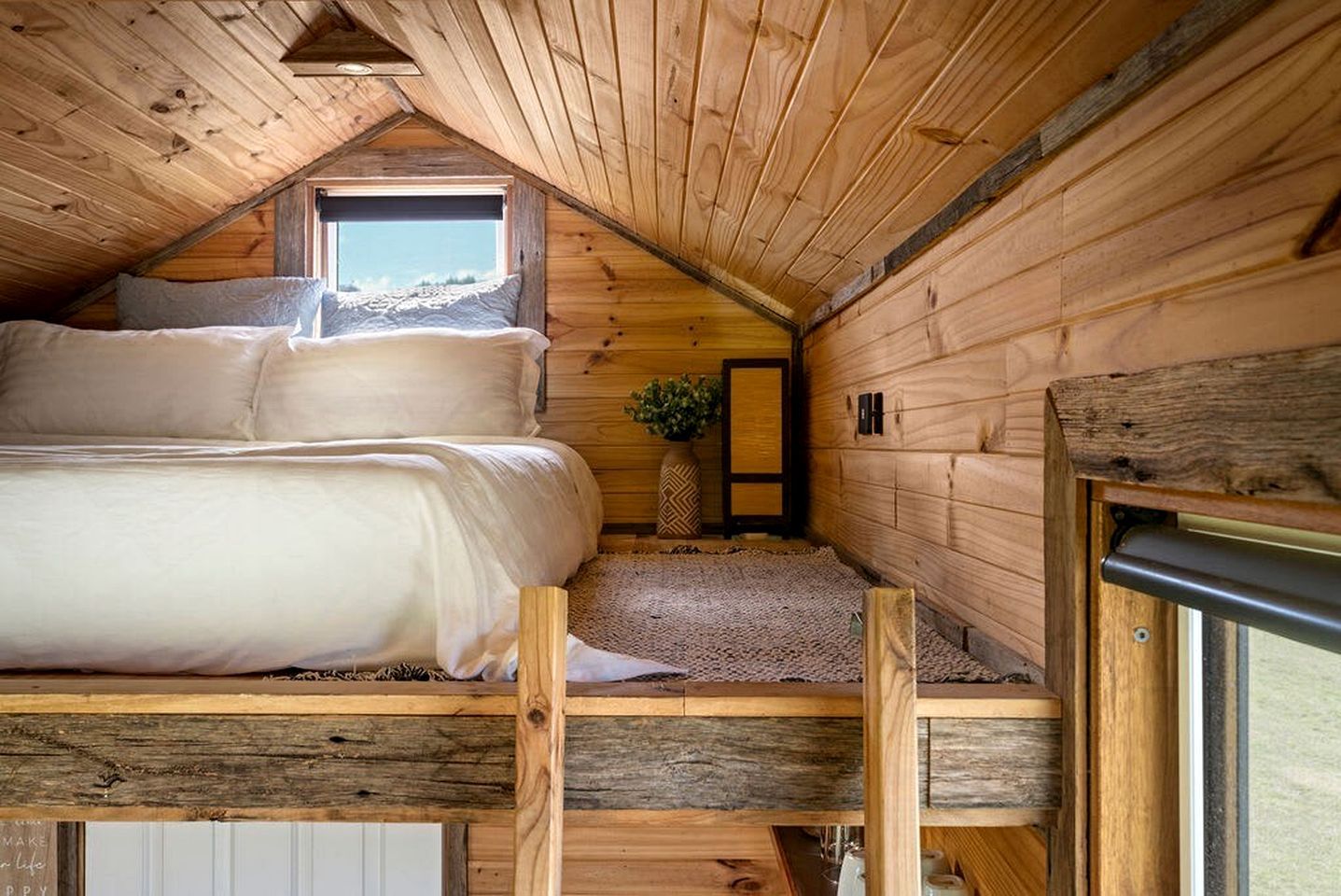 A cozy attic bedroom with a bunk bed, a small window, and wooden walls.