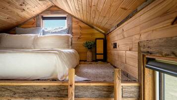 A cozy attic bedroom with a bunk bed, a small window, and wooden walls.