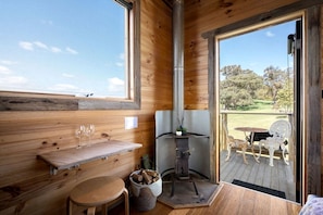 Un intérieur en bois avec une cheminée, un banc en bois, une table avec des verres et une vue sur l’extérieur.