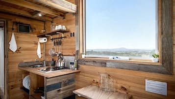 Una cocina rústica con paredes de madera, un ventanal con vistas y comodidades básicas como una tetera y utensilios.