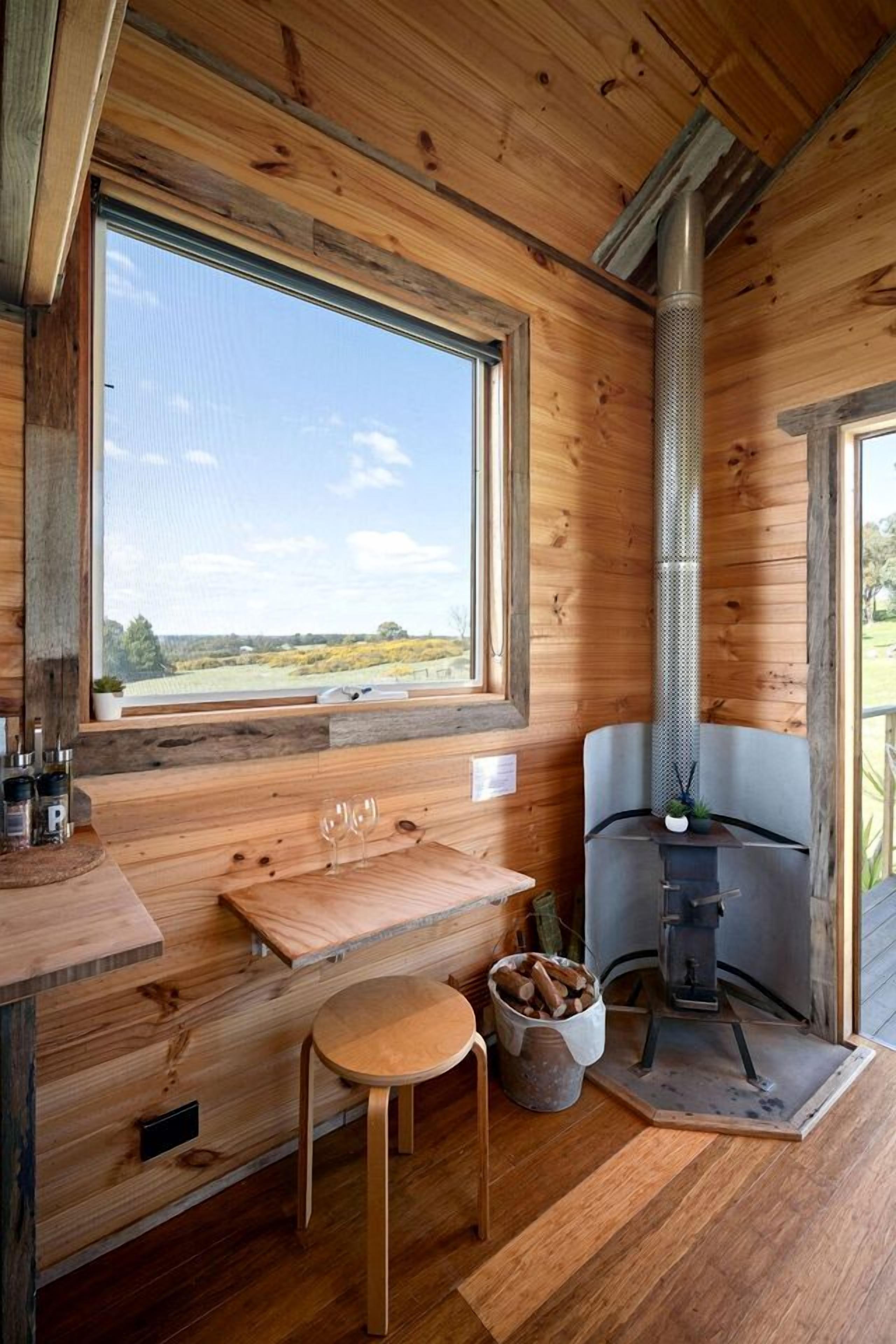 A wooden interior with a large window, a fireplace, a table, and a chair.