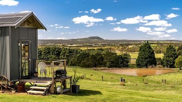A rustic cabin with a deck, a small pond, and a view of rolling hills.