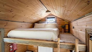 A small, wooden attic bedroom with a bunk bed, a window, and a fire extinguisher.