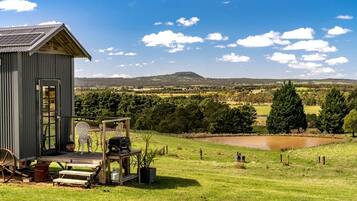 A rustic cabin with a deck, a small pond, and a view of rolling hills.