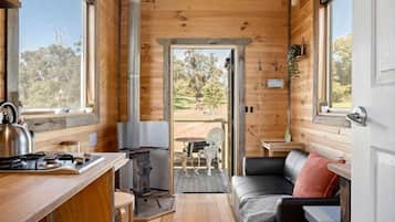A compact wooden cabin interior with a kitchenette, seating area, and a view through a door.