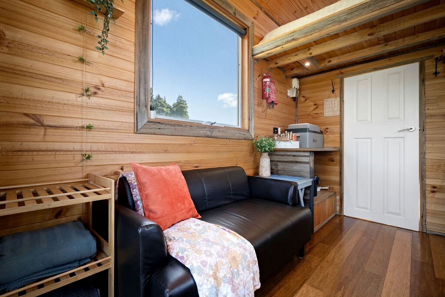 Un interior de madera con un sofá de cuero negro, una puerta blanca y una ventana.