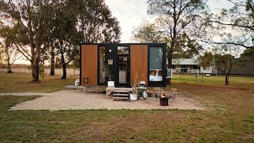 A modern, compact cabin with a wooden exterior, a small porch area, and a fire pit.