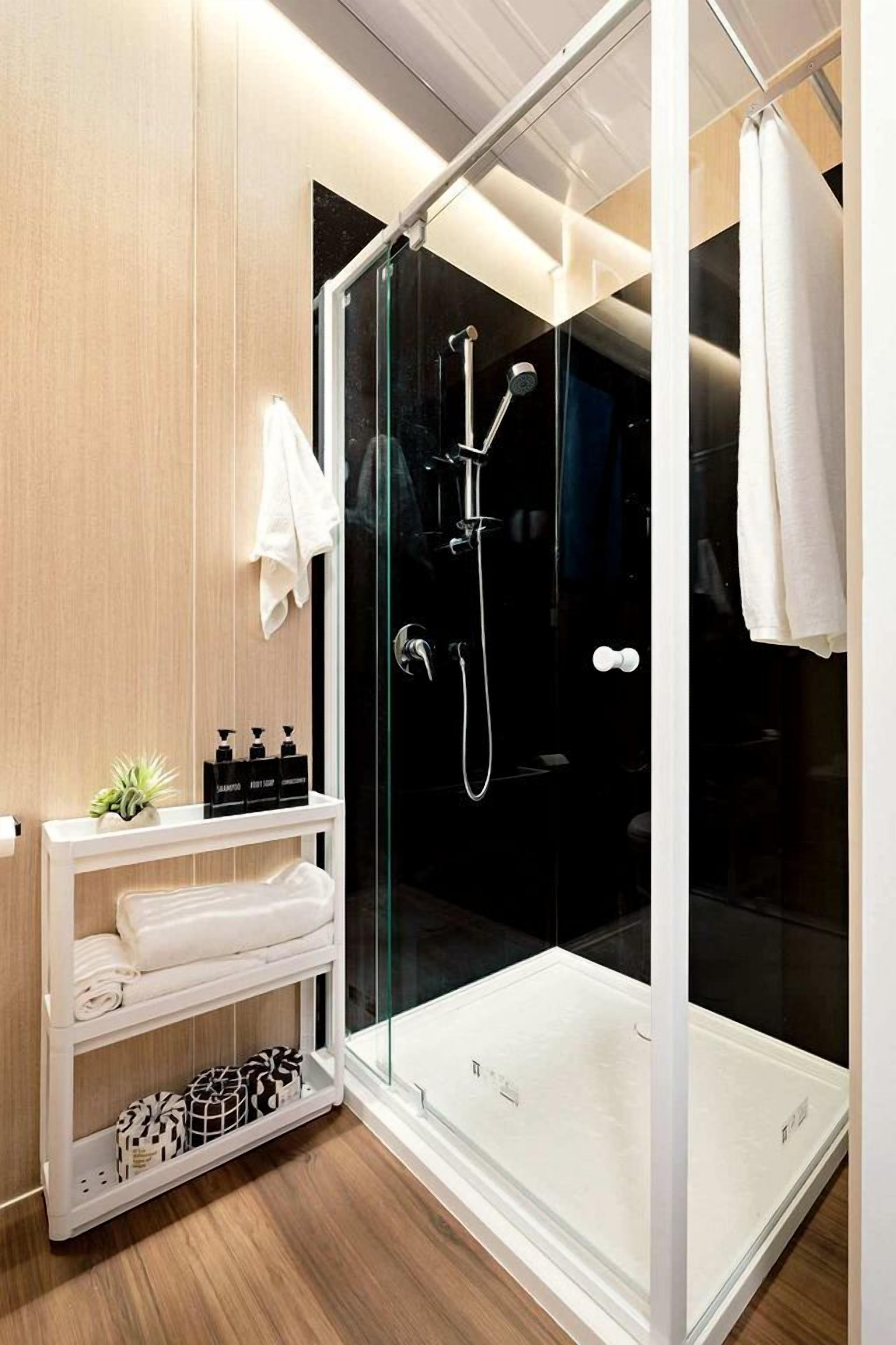 Ein modernes Badezimmer mit einer begehbaren Glasdusche, einem weißen Waschtisch mit Toilettenartikeln und einem Holzboden.