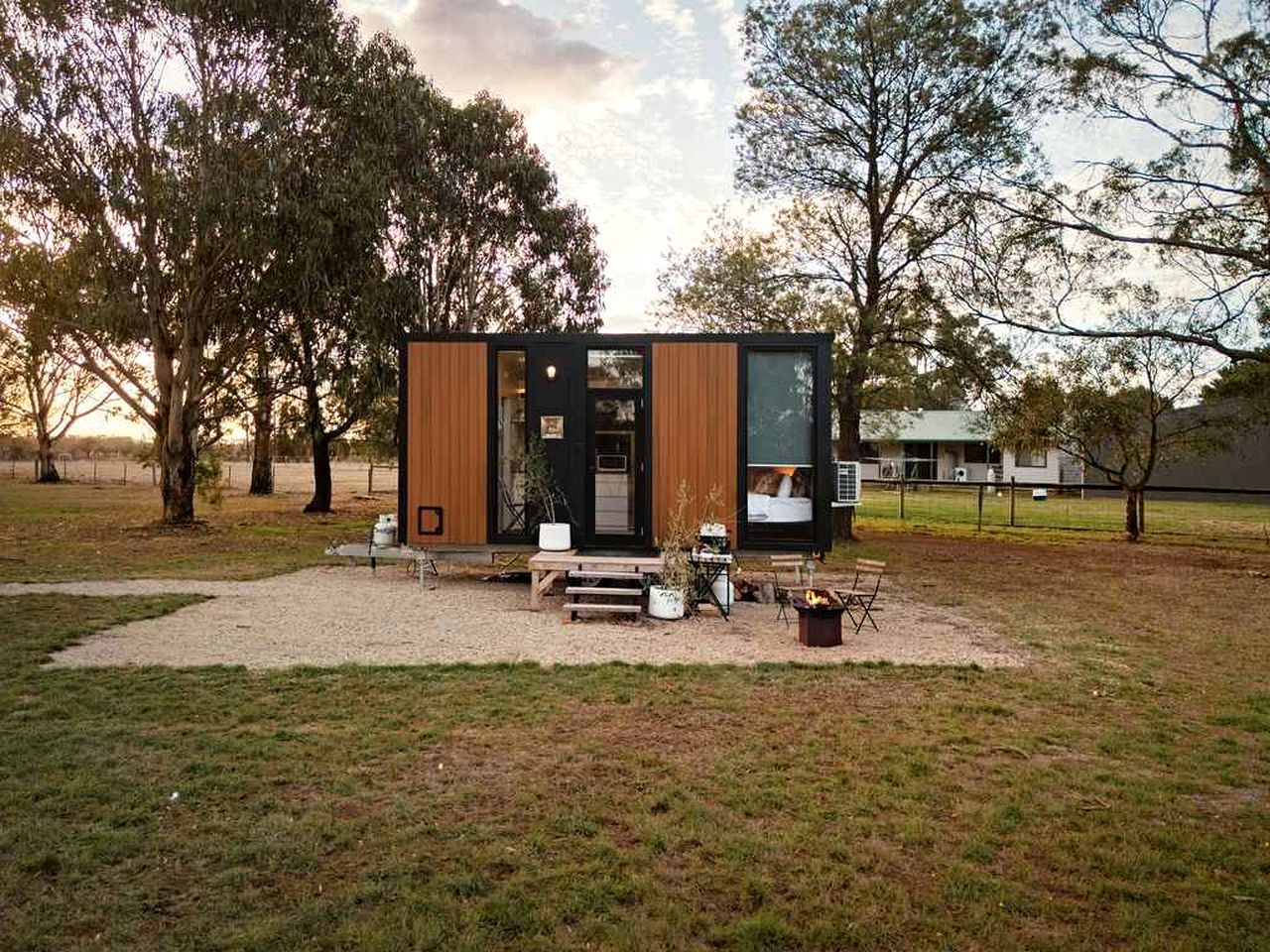 A modern, compact cabin with a wooden exterior, a small porch area, and a fire pit.