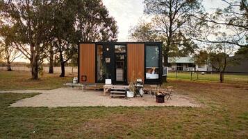 A modern, compact cabin with a wooden exterior, a small porch area, and a fire pit.