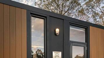 A modern exterior with a wooden panel facade, a black door with glass panels, and a small potted plant on a wooden stand.