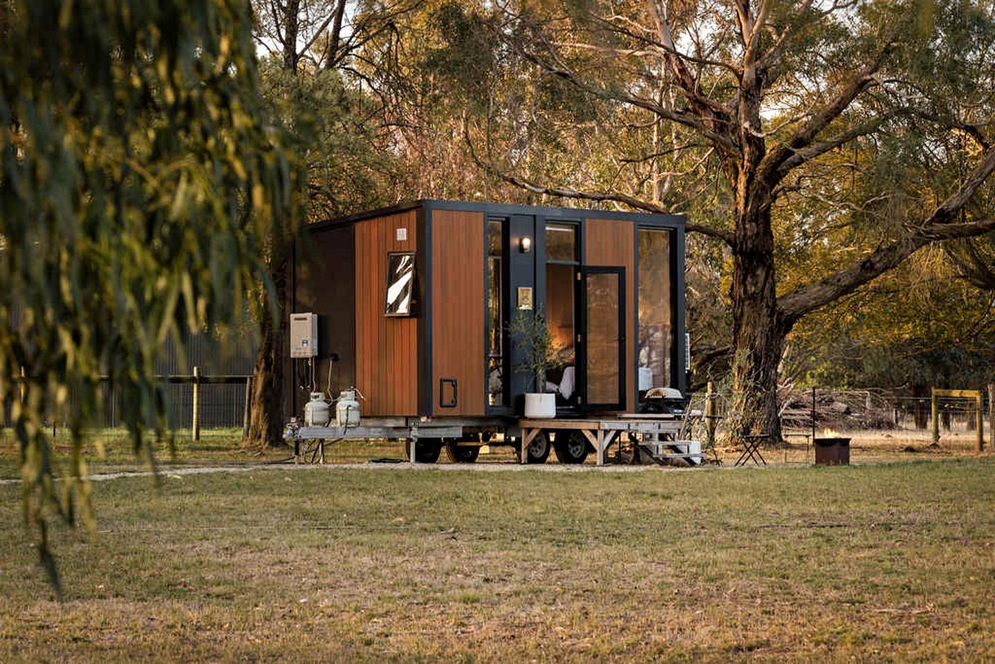 Een klein, laag huis met een plat dak, gelegen op een grasveld met bomen op de achtergrond.