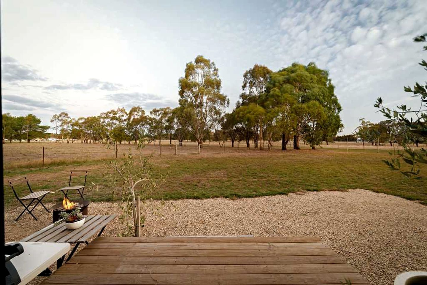 A wooden deck with outdoor seating and a fire pit, surrounded by a grassy field and trees.