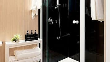 A modern bathroom with a glass-enclosed shower, a white vanity with toiletries, and a wooden floor.