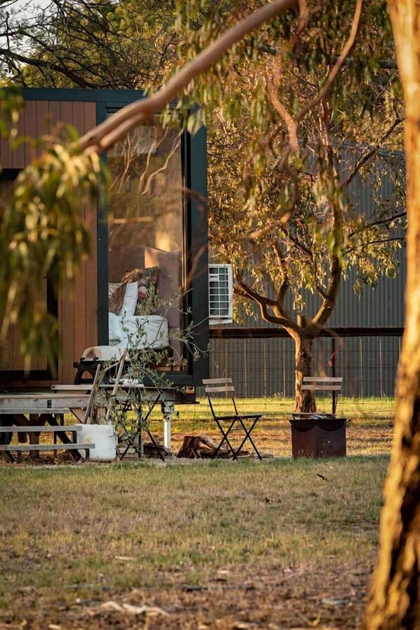 Un espace extérieur aménagé avec des bancs et une table, entouré d’arbres et d’un bâtiment doté d’une fenêtre.