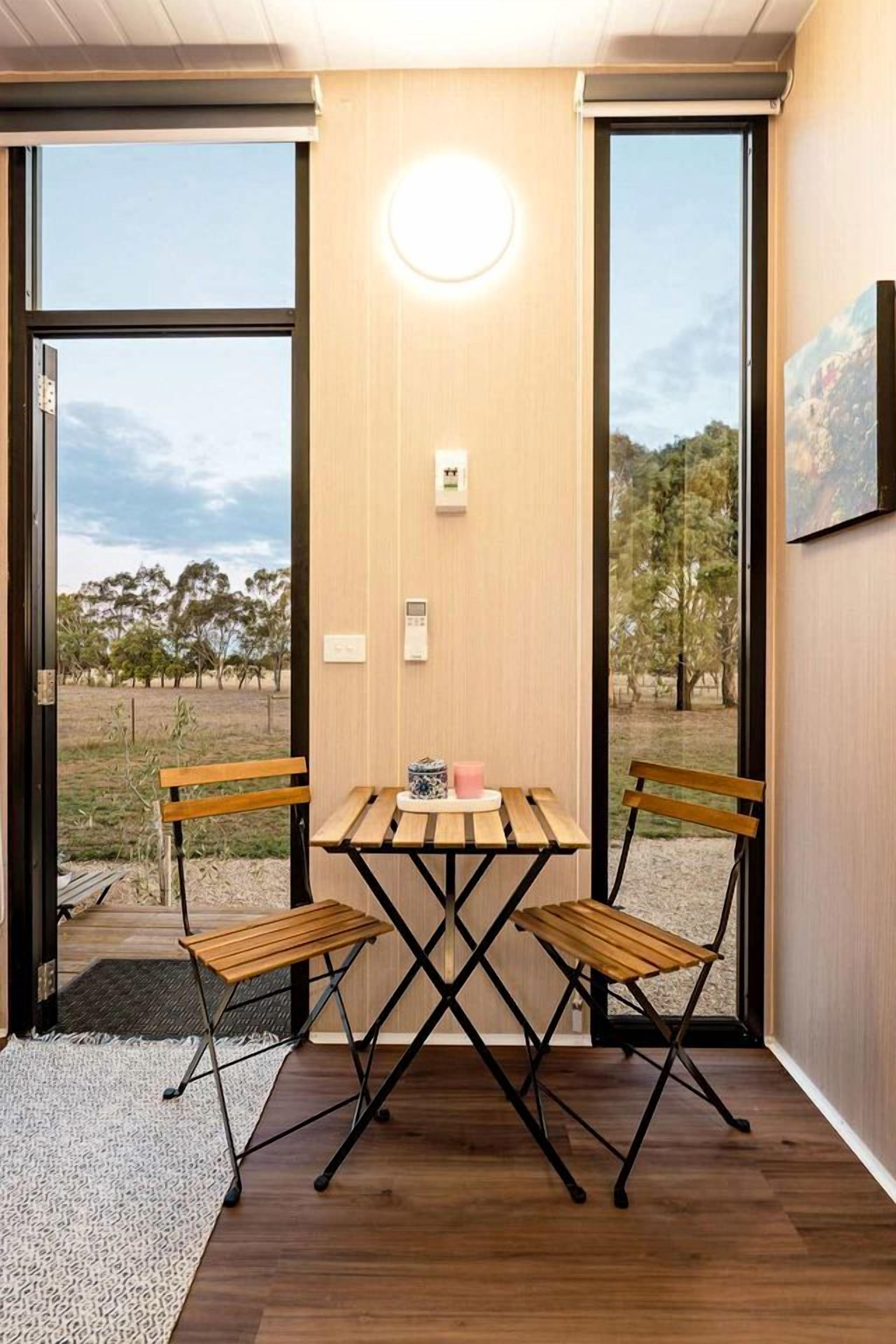 A room with a wooden table and two chairs, a door leading outside, and a wall-mounted light fixture.