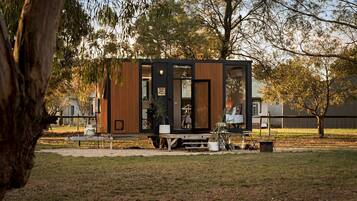 A modern, compact cabin with a large sliding door, a small porch area, and a visible interior with a bed and seating.