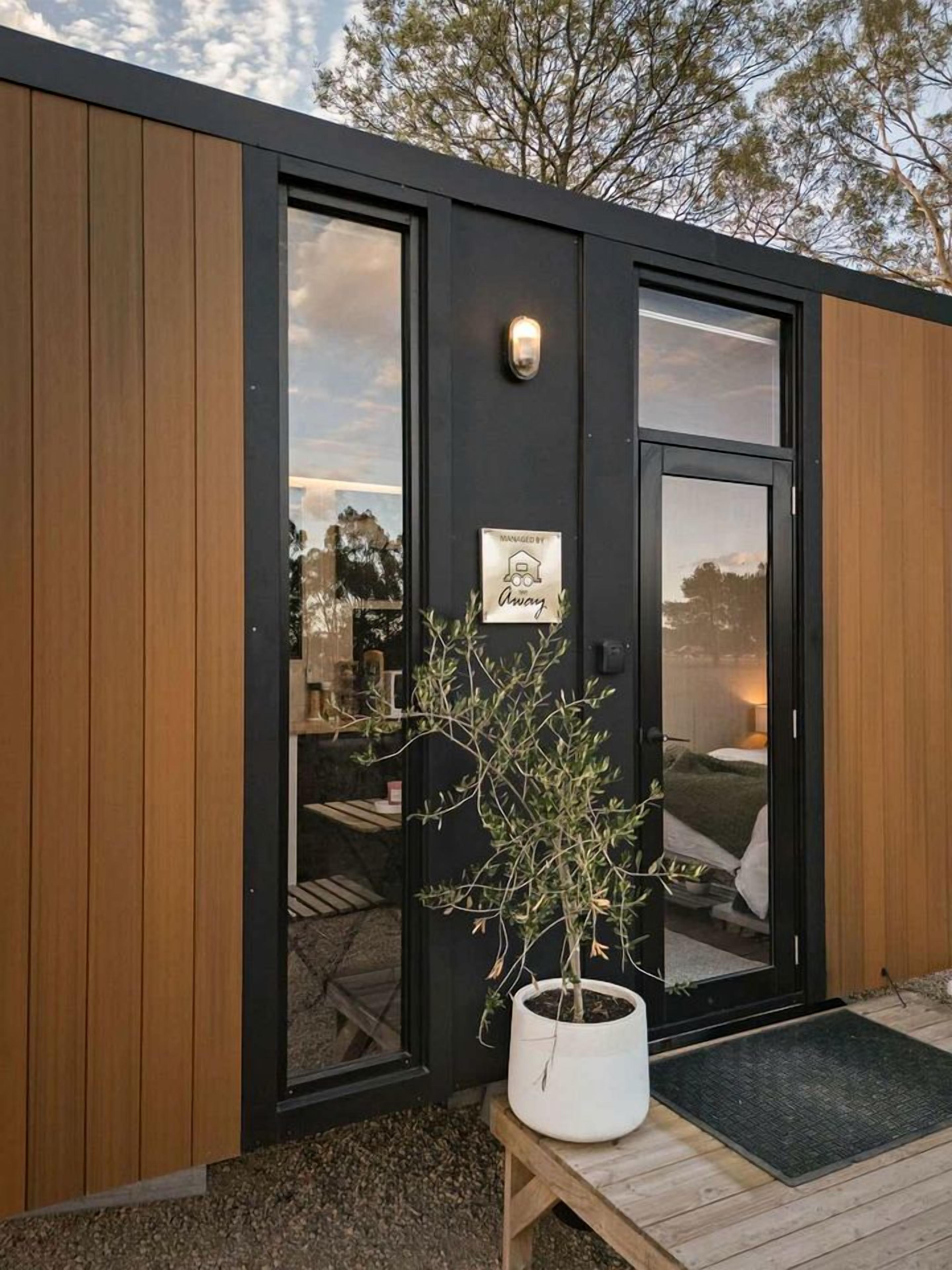 A modern exterior with a wooden panel facade, a black door with glass panels, and a small potted plant on a wooden stand.