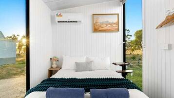 Ein Schlafzimmer mit einem Bett, Kissen, einem Nachttisch, einer Wand-Klimaanlage und einem Bild.