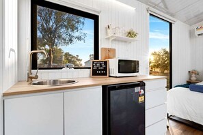 Cocina compacta con lavamanos, microondas y refrigerador. Se ve una ventana con vistas a árboles y cielo despejado.