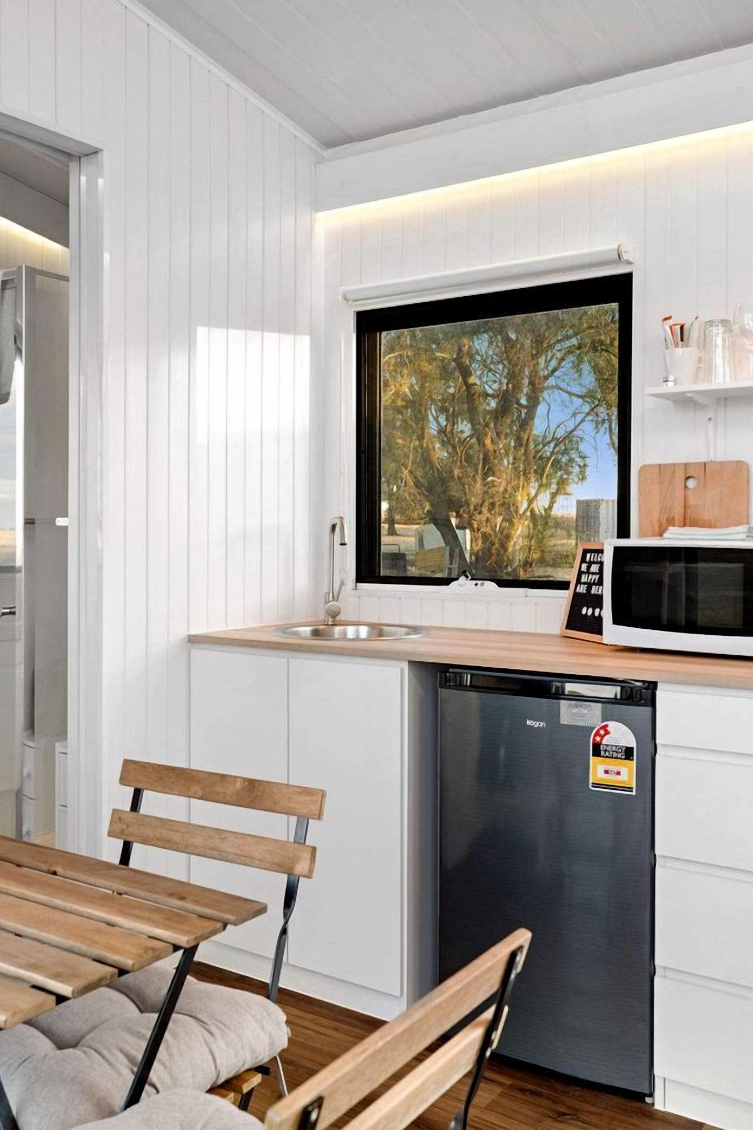 Una cucina moderna con mobili bianchi, un piano di lavoro in legno, una lavastoviglie integrata e una finestra vista alberi.