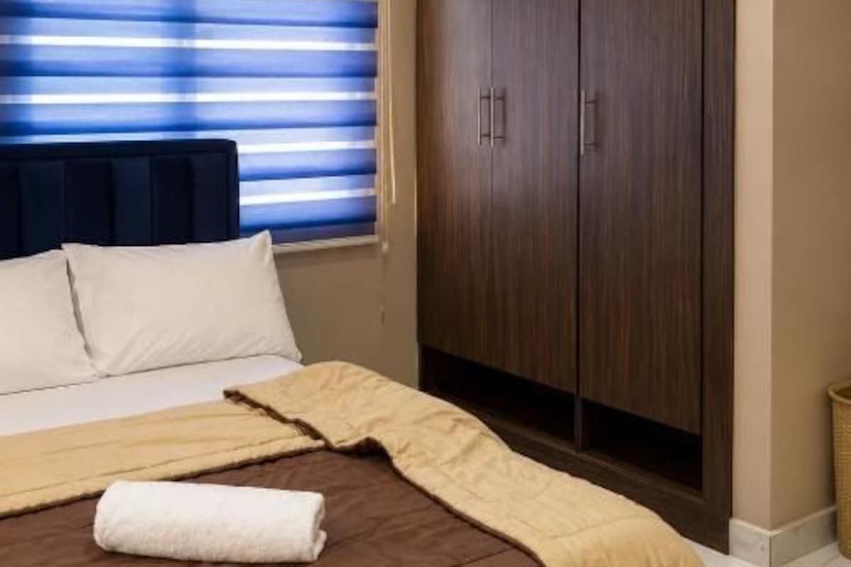 A hotel room with a bed, a wardrobe, and a window with blinds.