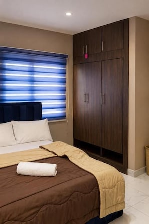A hotel room with a bed, a wardrobe, and a window with blinds. - Caligeo Suites I (Ibadan)