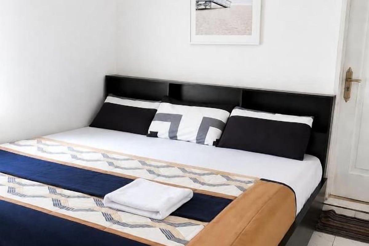 A neatly made bed with a patterned bedspread, a black headboard, and a framed picture on the wall.