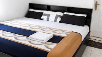 A neatly made bed with a patterned bedspread, a black headboard, and a framed picture on the wall.