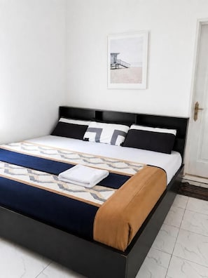 Cama bem arrumada com colcha estampada, cabeceira preta e quadro na parede.