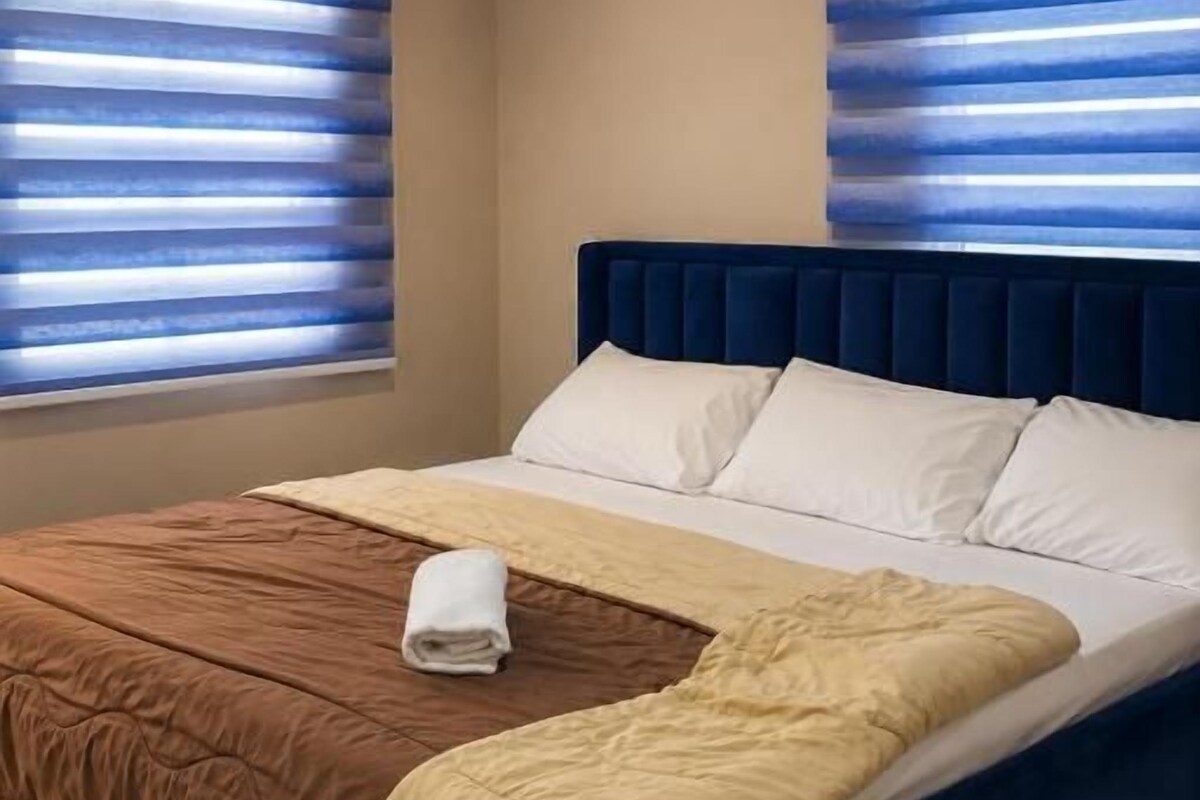 A bedroom with a bed, two windows with blinds, and a headboard.