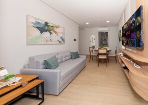 A modern living room with a grey sofa, a dining table with chairs, and a wall-mounted TV displaying various channels. - Corporate Stays Matrisa - 1003 (Asunción)