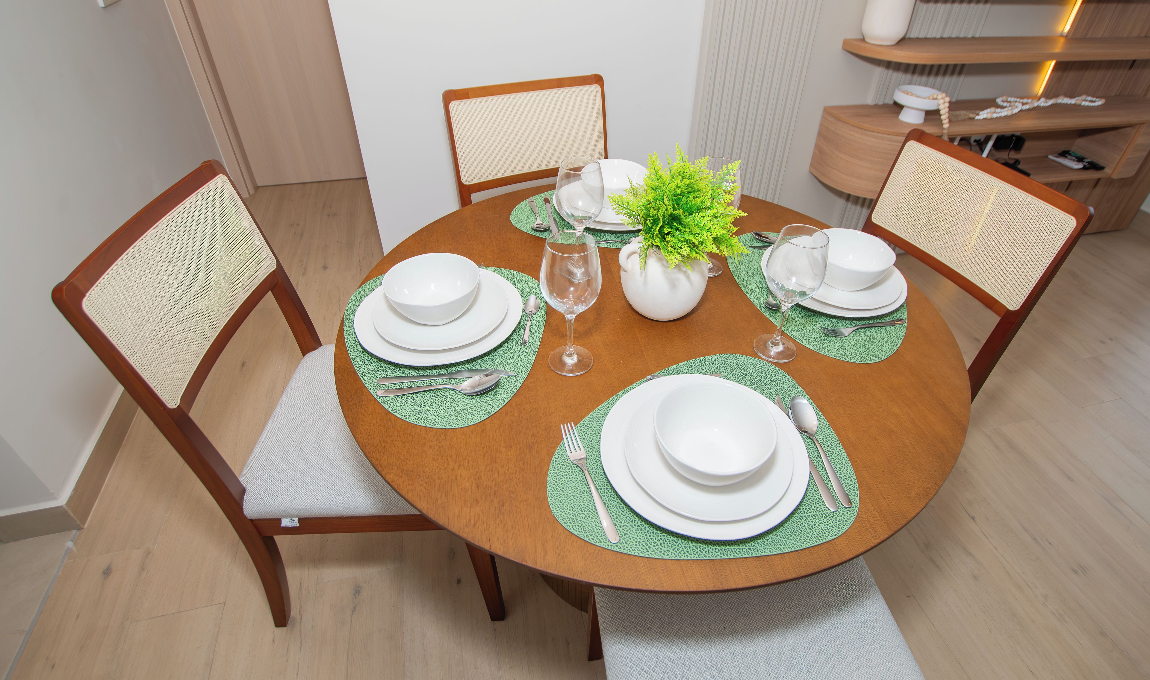 Una mesa de comedor redonda con platos blancos, individuales verdes y cubiertos.
