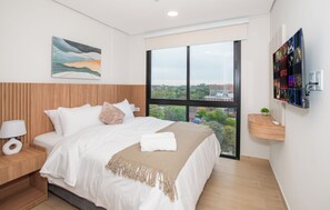 A modern hotel room with a large bed, a painting on the wall, a TV mounted on the wall, and a view of the city through the window. - Corporate Stays Matrisa - 1003 (Asunción)