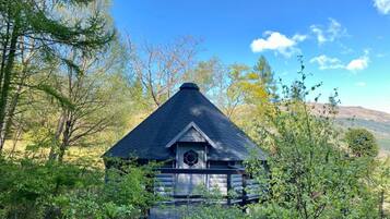 Eine Blockhütte mit einem steilen Satteldach, umgeben von dichtem Wald und Hügeln im Hintergrund.