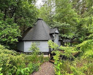 A cabin with a hexagonal roof, surrounded by dense greenery.
