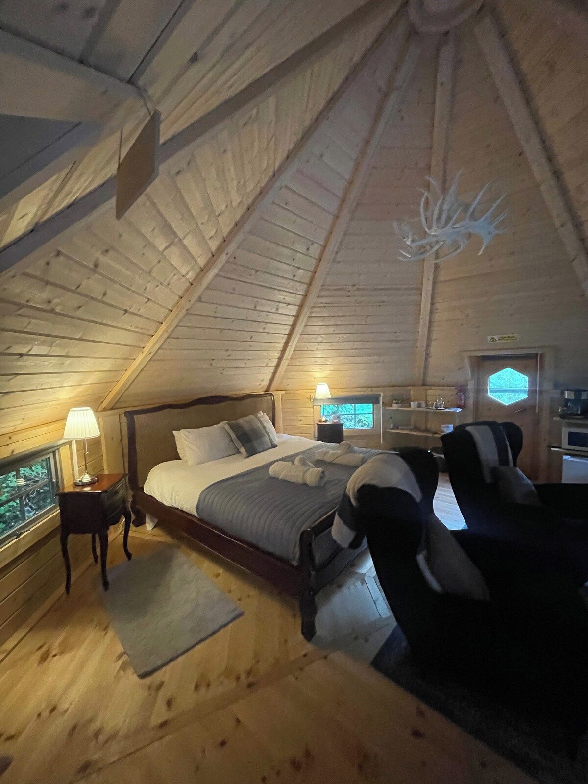Ein gemütliches Schlafzimmer mit schrägen Wänden, einem Bett mit Kissen, einem Nachttisch mit Lampe und einem Sessel.