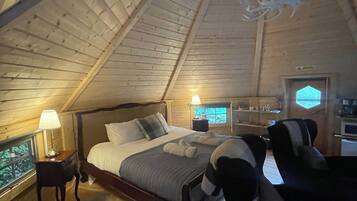 Ein gemütliches Schlafzimmer mit schrägen Wänden, einem Bett mit Kissen, einem Nachttisch mit Lampe und einem Sessel.