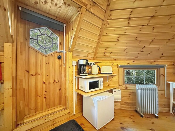 Ein gemütliches Holzhaus-Interieur mit Tür, Fenster, Mikrowelle, kleinem Kühlschrank und Heizkörper.