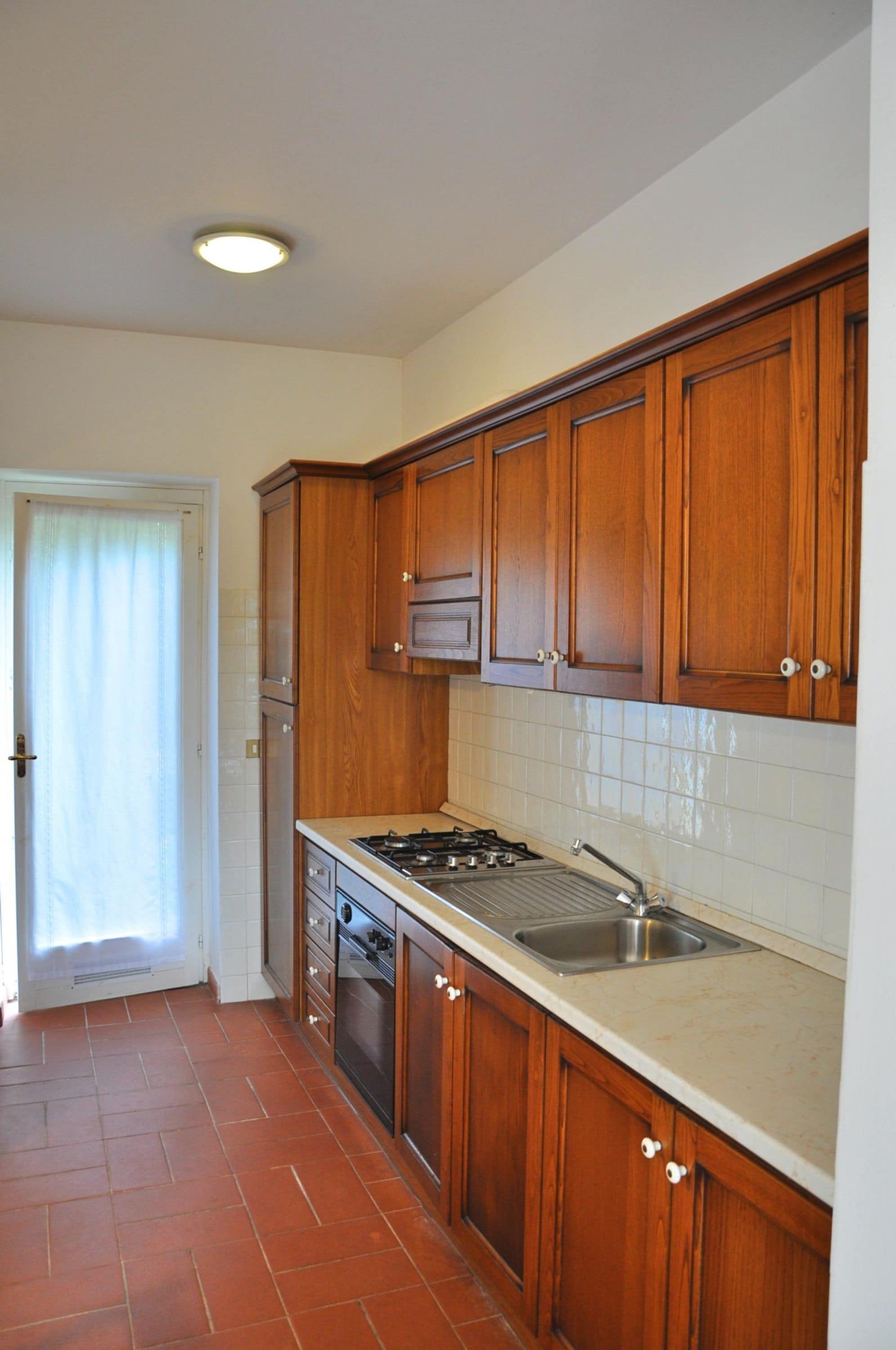 A kitchen with wooden cabinets, a gas stove, and a stainless steel sink.
