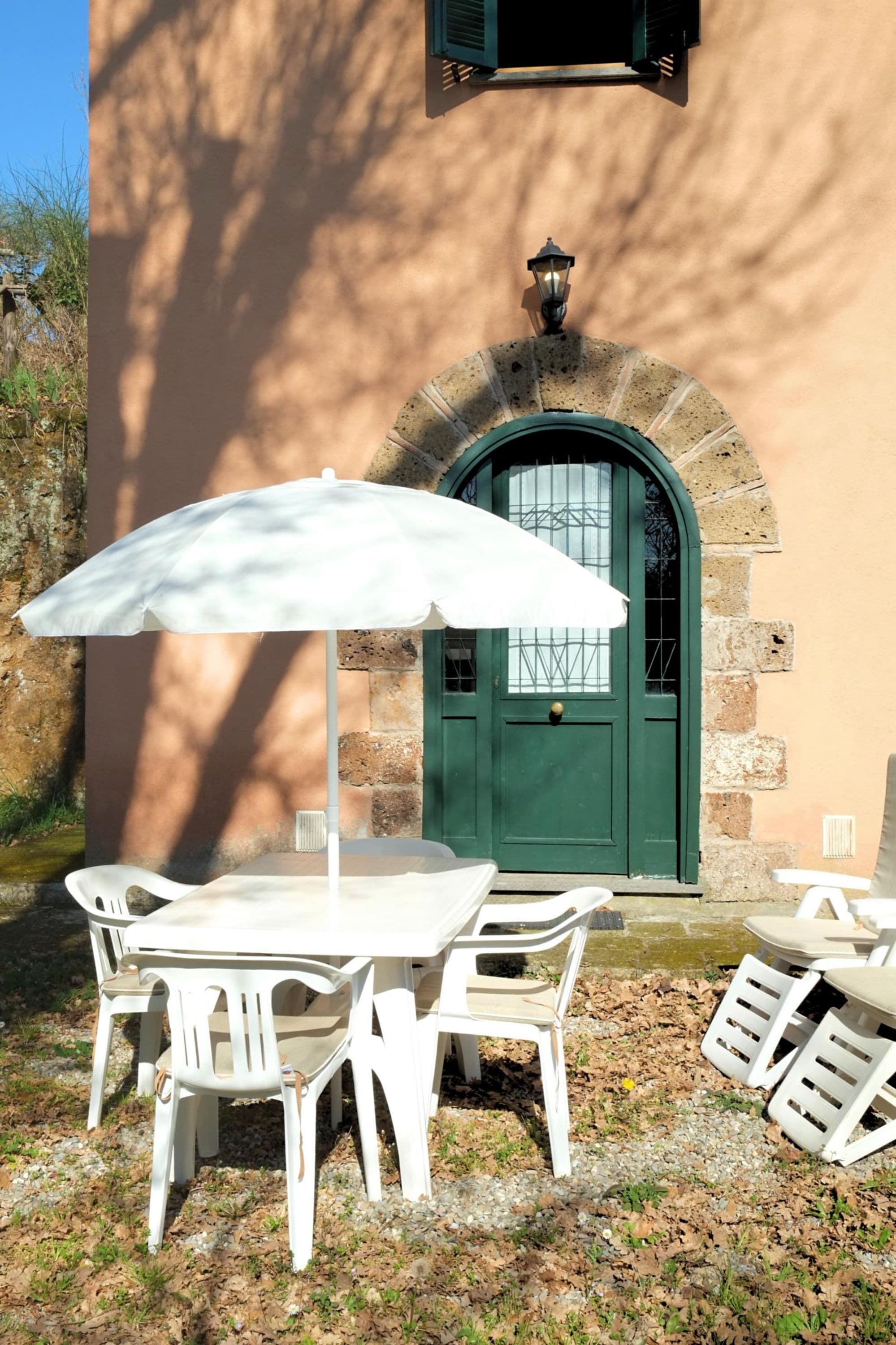 A patio with a table and chairs, an umbrella, and a building with a green door and stone architecture.
