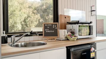 A kitchen with a sink, a coffee maker, a toaster, a microwave, and a sign that reads 'WELCOME TO JBJK HOMESTEAD'.