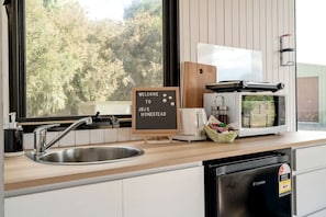 A kitchen with a sink, a coffee maker, a toaster, a microwave, and a sign that reads 'WELCOME TO JBJK HOMESTEAD'.