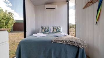 A room with a bed, pillows, a blanket, and an air conditioning unit.