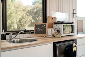 A kitchen with a sink, a coffee maker, a toaster, a microwave, and a sign that reads 'WELCOME TO JBJK HOMESTEAD'. - Victoria Tiny House for Couples Glamping on a Homestead (Gobur)