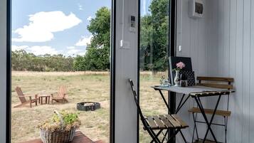 A room with a view of a grassy field, a wooden table with chairs, and a small garden outside.
