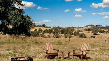 Two wooden chairs in a grassy field with a tree and hills in the background.